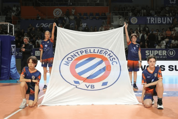 Quatre jeunes enfants brandissent un drapeau avec le logo de Montpellier avant un match. (Montpellier Volley-Ball)